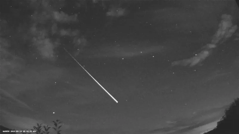 A dark sky with a few clouds and a a bright fireball streak in the middle