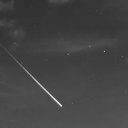 A dark sky with a few clouds and a a bright fireball streak in the middle