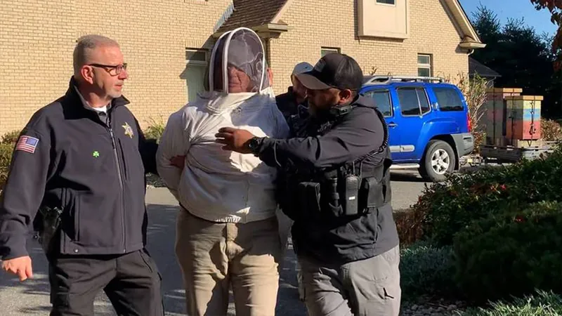 A woman in a full beekeeper suit is led away from a house by police officers.