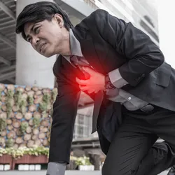 Man in suit bent over on pavement clutching his chest