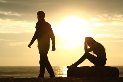 silhouette of couple breaking up against a sunset on the beach