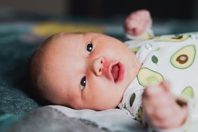 A newborn baby is resting in a crib, with avocados on its body suit. 