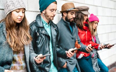 five people with their backs against a wall looking at their phones