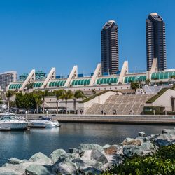 San Diego convention center as seen from the Embarcadero South. Conference building in front of a harbour with boats. Large business buildings in the back. 