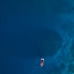 a tiny boat over the shadow of a massive coral