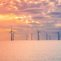 an image of the calm sea with a cloudy sky. on the horizons dozens of widn turbines are visible