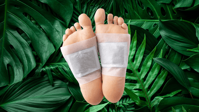 photograph of feet that have teabag-like patches stuck to them, against a background of dark green leaves