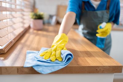 Close up of a gloved hand wiping a kitchen surface with a microfiber cloth.