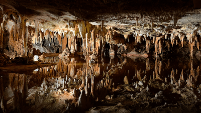 a cave lit up shows stalagmites growing up from the floor and stalactites dropping down from the ceiling