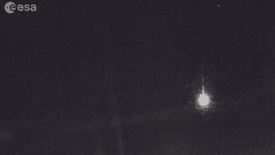 A grainy view of the sky with a bright light followed by a thin tail.