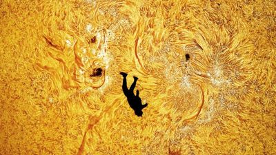 the silhoutted of a skydiver is captured in front of the turbuletnt sun where multiple sunspots are visible.