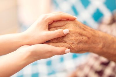 younger person with painted nails holding the hands of an elderly person