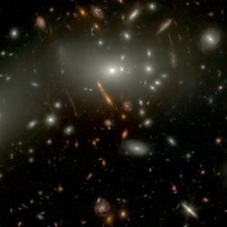 On a black background many galaxies are visible. The brighetest and closest are large and shine bright. Many small red galaxies are seen, among them , highlighted in an inset is Alaknanda. The inset show that it has a core and spiral arms.