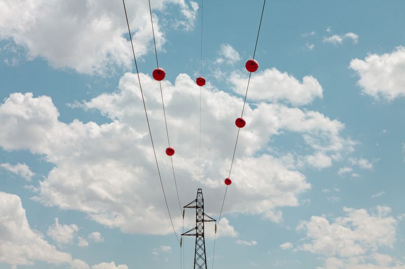 Electric power transmission lines with red marker balls and a background of beautiful cloudy sky.