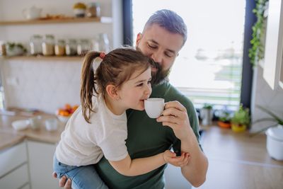 father holding up a small coffee cup to his daughter's mouth