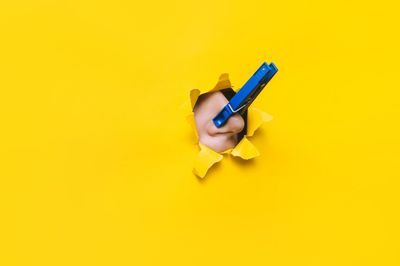 nose with blue clothespin on it breaking through hole in yellow paper