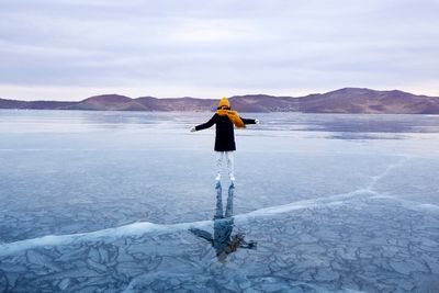 woman on frozen lake skating, wearing a black coat and yellow hat and scarf