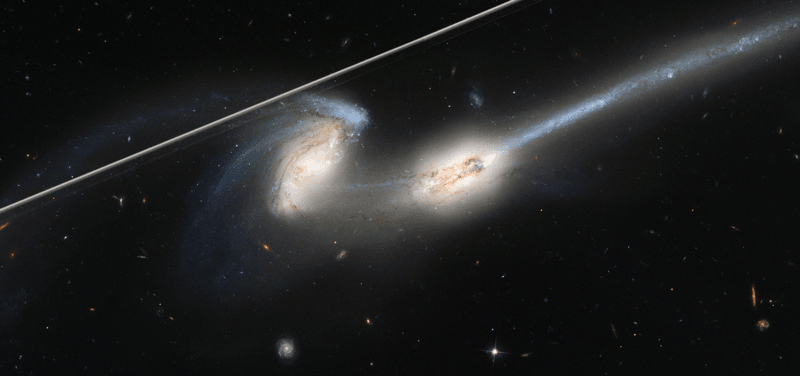 A picture of the interacting pair of galaxies knwon as the mice, where two spiral galaixes are in the process of merging. One of them has a spiral arm stretched into a long tail. A broad white streak cuts the image, that's the satellite trail.