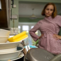 A woman looks at a sink full of dishes,