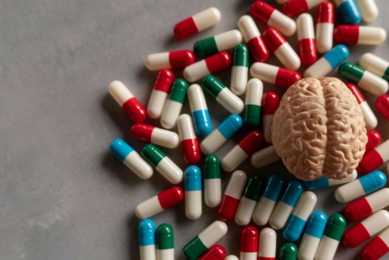 small 3D model of a brain on a pile of different coloured pill capsules, on a table