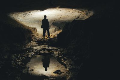 man's silhouette reflecting in water in dark cave