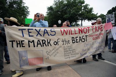 A photo showing a group of protestors holding a large sheet as a banner saying "Texas will not take the mark of the Beast" as part of an ant-vaccination march.