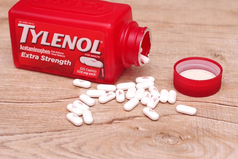 red bottle of extra strength tylenol open on a wooden table with white pills spilling out