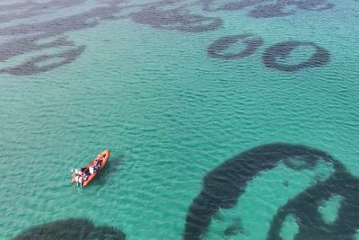 A orange dingy is in the middle of clear blue seas. Periodically there are darker rings of seagrass that can be seen under the water.