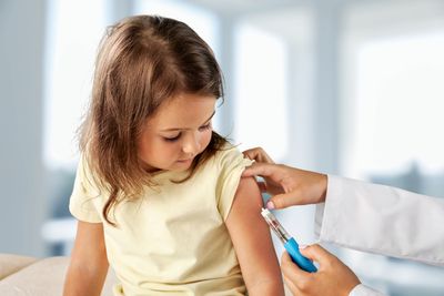 Medical professional injecting a vaccine into the arm of a young girl, who is looking down at her arm