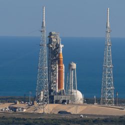 A picture from the distance showing the rocket and the other structures around the launch pad. Behind is the ocean.