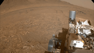 an image of the back of the rover with behind the tracks in the sand of Mars. 