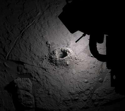 A large drilled hole on a rock with Curiosity's LEDs lighting it up.