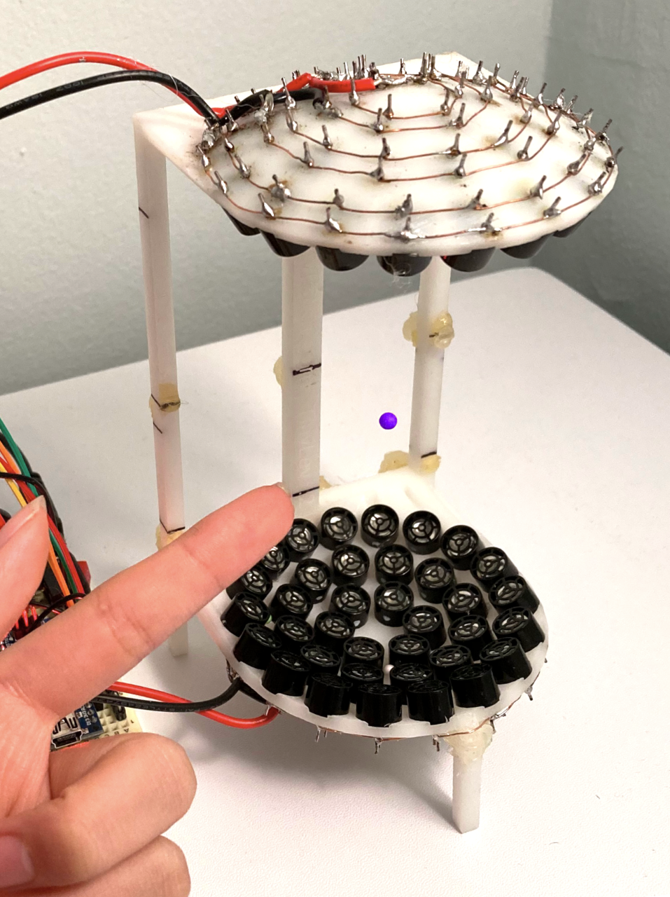two semicircular structures with mini sounds speakers keeping a purple bead levitating.