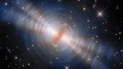  In the centre an opaque cloud of grey gas hides a star. Two strong beams of light from the star emerge from large holes in both sides of the cloud. The central cloud is surrounded by concentric, wispy shells of gas, illuminated by the star’s light. The shells reflect extra light where they’re hit by the twin beams. A crowd of smaller stars with cross-shaped spikes over them surround the nebula on a black background