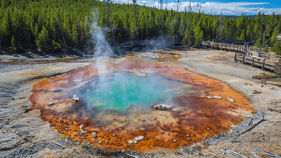 Echinus geyser at Yellowstone National Park. A red pool with a blue-green center, with steam coming off the surface.