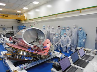 a group of 10 individuals all covered in the clean room standing next to the full scale build up of the spacecraft.