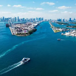 An aerial view of a the port of Miami with shipping boats and large buildings in the background.