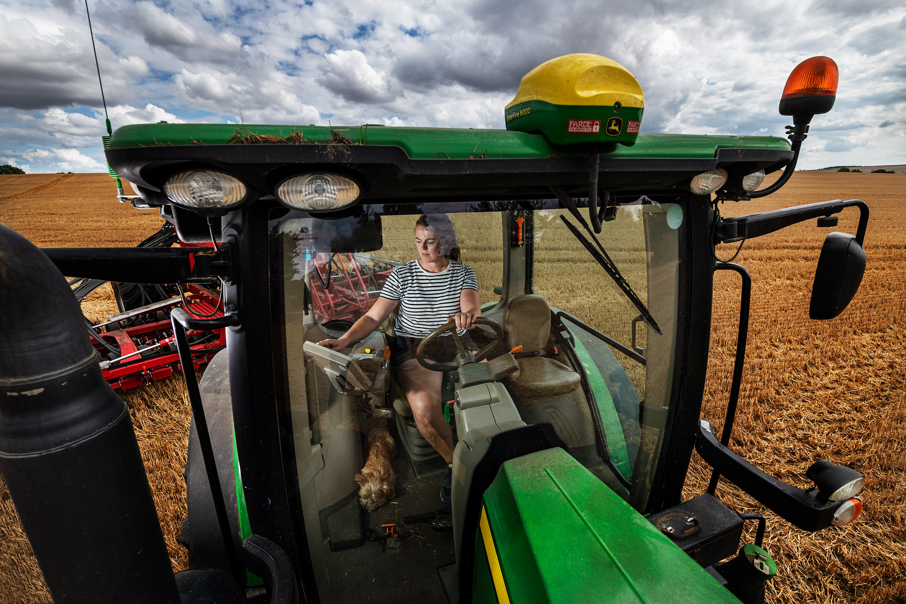 A woman is driving a tractor and using a table conected to satellites to perform agricultural duties