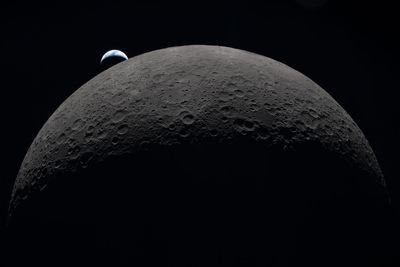 the far side of the Moon looms large as a crescent of Earth is visible far in the distance.
