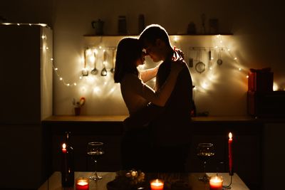 couple in kitchen embracing romantically surrounded by candles and fairy lights
