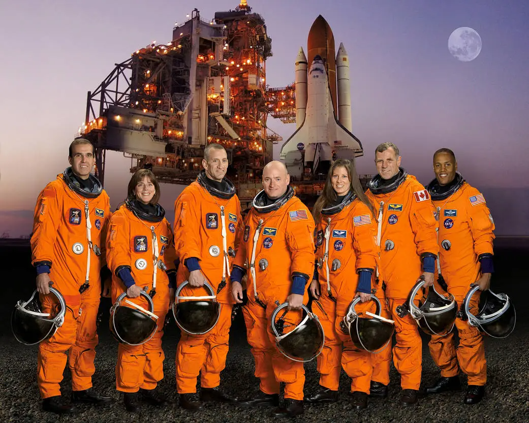 The seven astronauts pose in their orange suits with a picture of the space shuttle in the backgrouns The seven astronauts pose in their orange suits with a picture of the space shuttle in the backgrouns