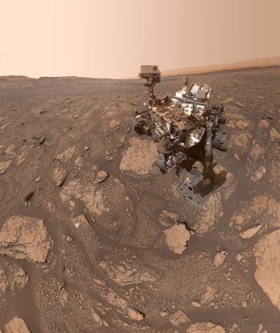 the rover is visible with a lot of red rocks and sand
