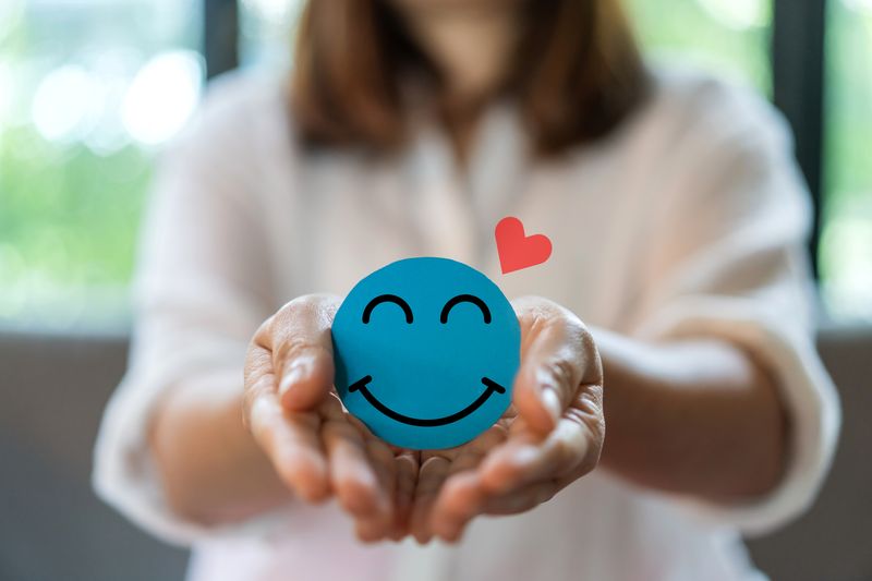 hands holding out a blue paper circle with a smiley face on it and red heart next to it