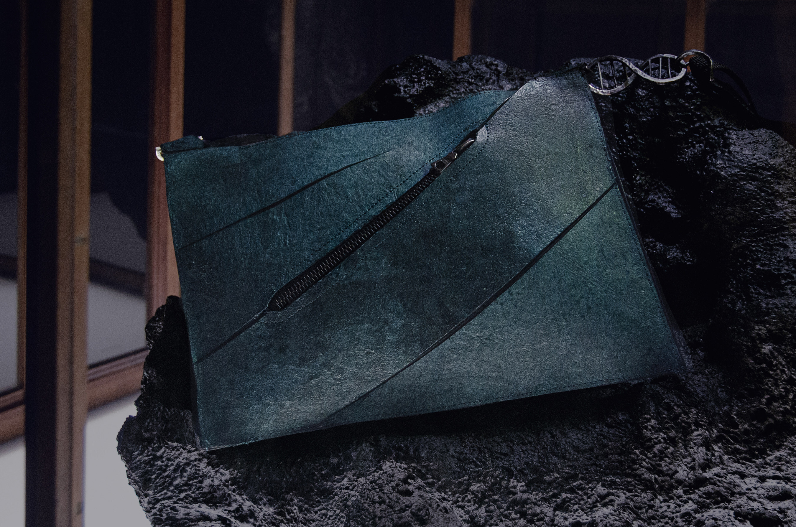 A teal blue handbag on a rock, with a zipper diagonally across the front.