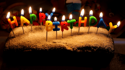 a birthday cake with lit candles that say happy birthday, the cake is covered in powdered sugar