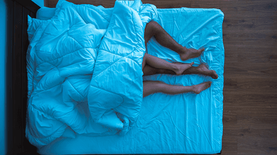 A couple in bed, with their legs poking out of the bottom of the duvet.