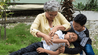 An older woman and a boy, tickling a second boy.