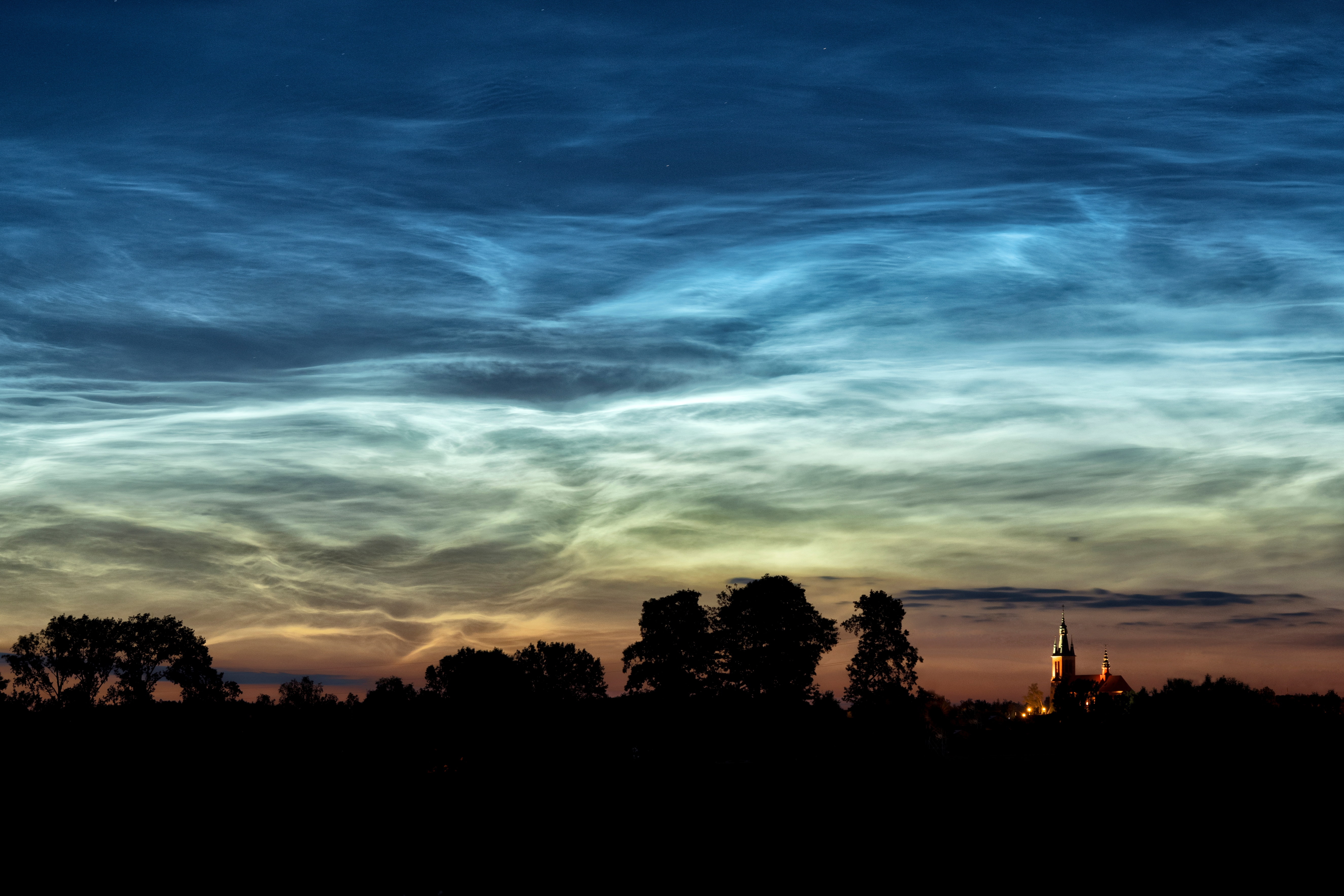 Noctilucent clouds seen in the sky over a countryside area. Noctilucent clouds seen in the sky over a countryside area.
