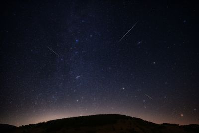 a dark hill silhoutte under the milky way and some meteor trails 