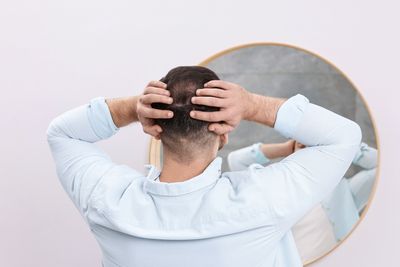 man examining hair in the mirror, viewed from behind